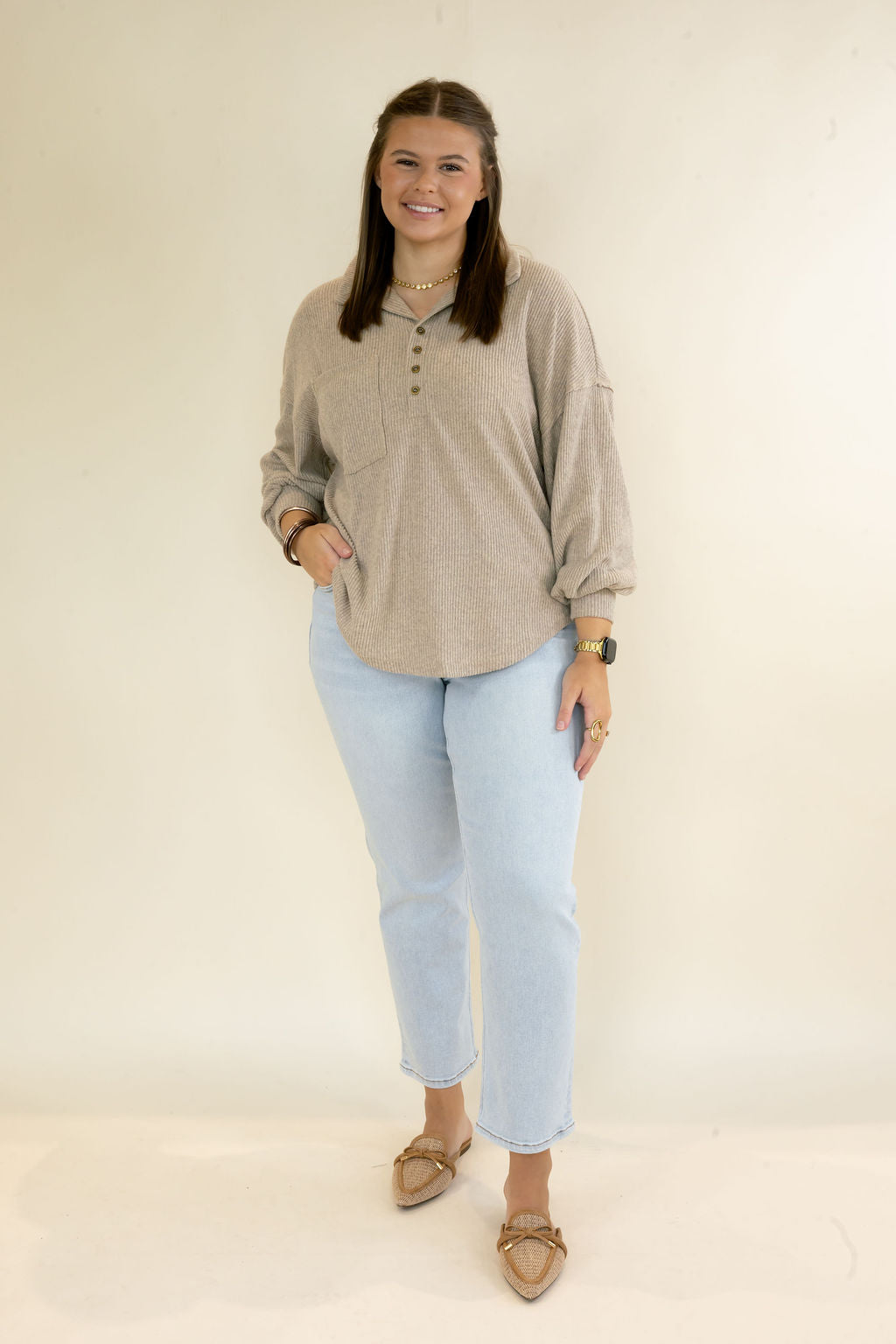 Woman modeling taupe ribbed collared pullover top with button neckline, front pocket, long sleeves, and relaxed fit styled with light wash cropped jeans and woven flats