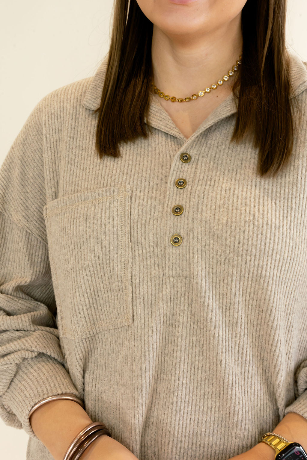 A close-up of a person wearing a ribbed knit long-sleeve polo shirt in a light taupe-beige color, featuring a buttoned collar and a chest pocket.