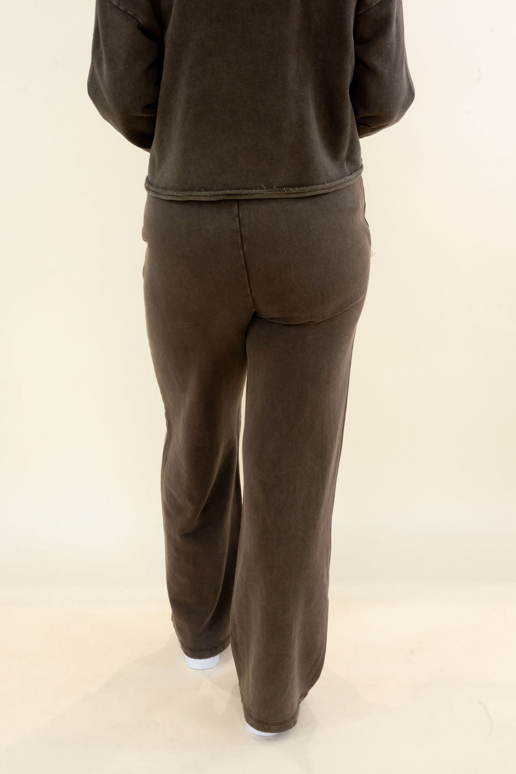 A person shown from the back wearing a matching dark brown lounge set consisting of a long-sleeve top and wide-leg pants, photographed against a plain off-white studio background.