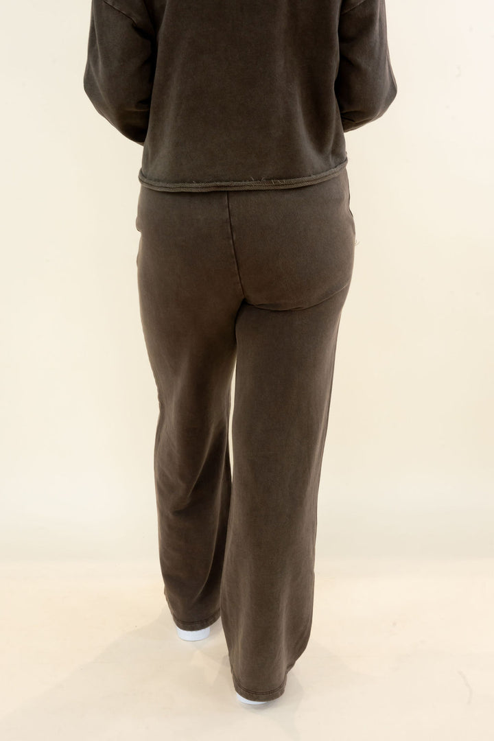 A person shown from the back wearing a matching dark brown lounge set consisting of a long-sleeve top and wide-leg pants, photographed against a plain off-white studio background.