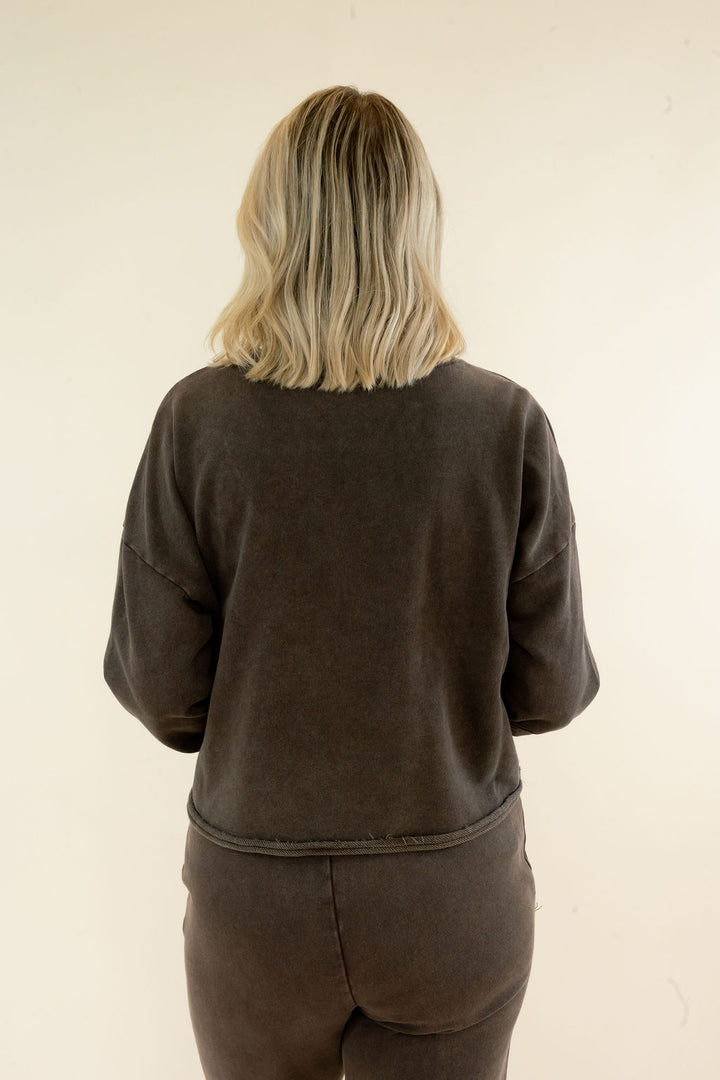 A person viewed from behind wearing a dark brown washed sweatshirt and matching sweatpants against a plain off-white background.