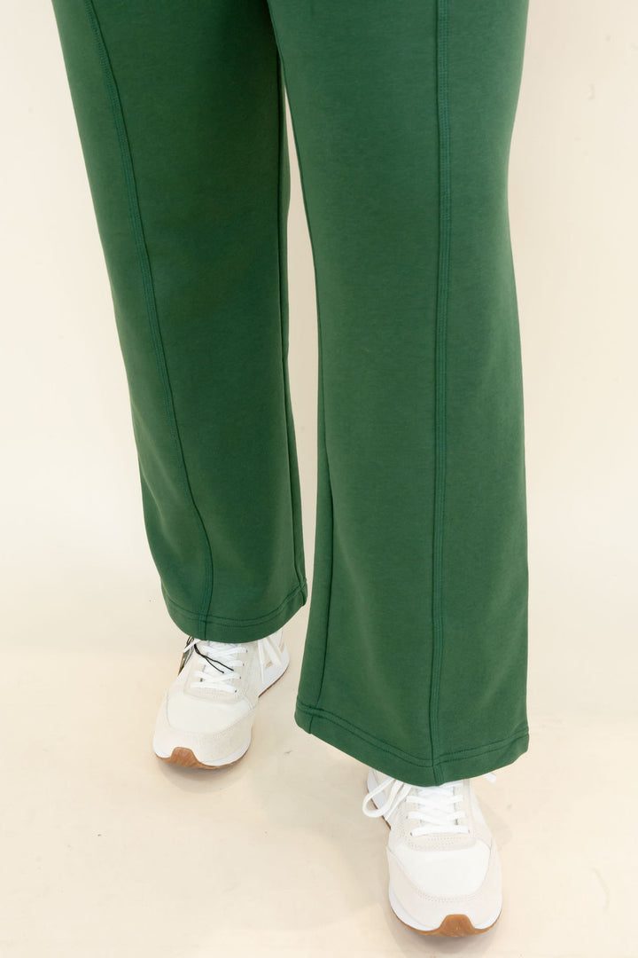 Green wide-leg sweatpants worn with white sneakers, shown from the thigh down against a plain light background.