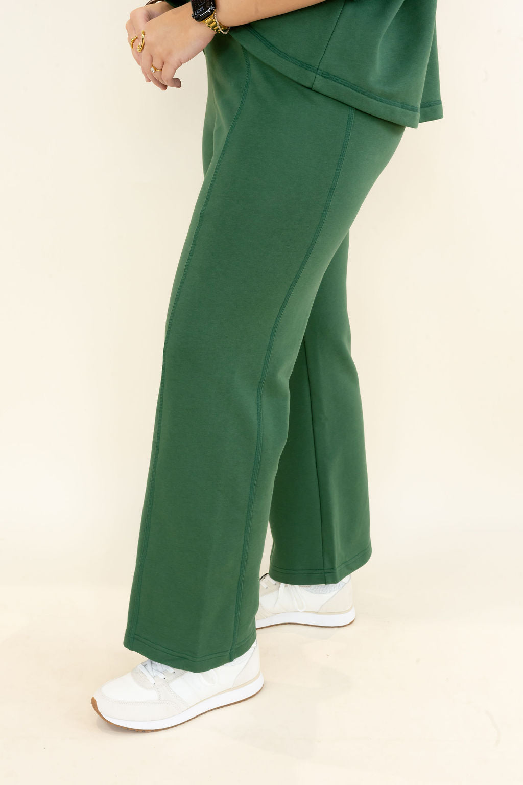 A person wearing dark green wide-leg sweatpants and white sneakers, shown from the waist down against a plain cream studio background.