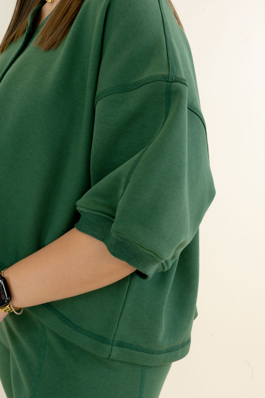 A close-up of a person wearing an oversized dark green top with ribbed cuffs and a matching green top, photographed against a plain light background.