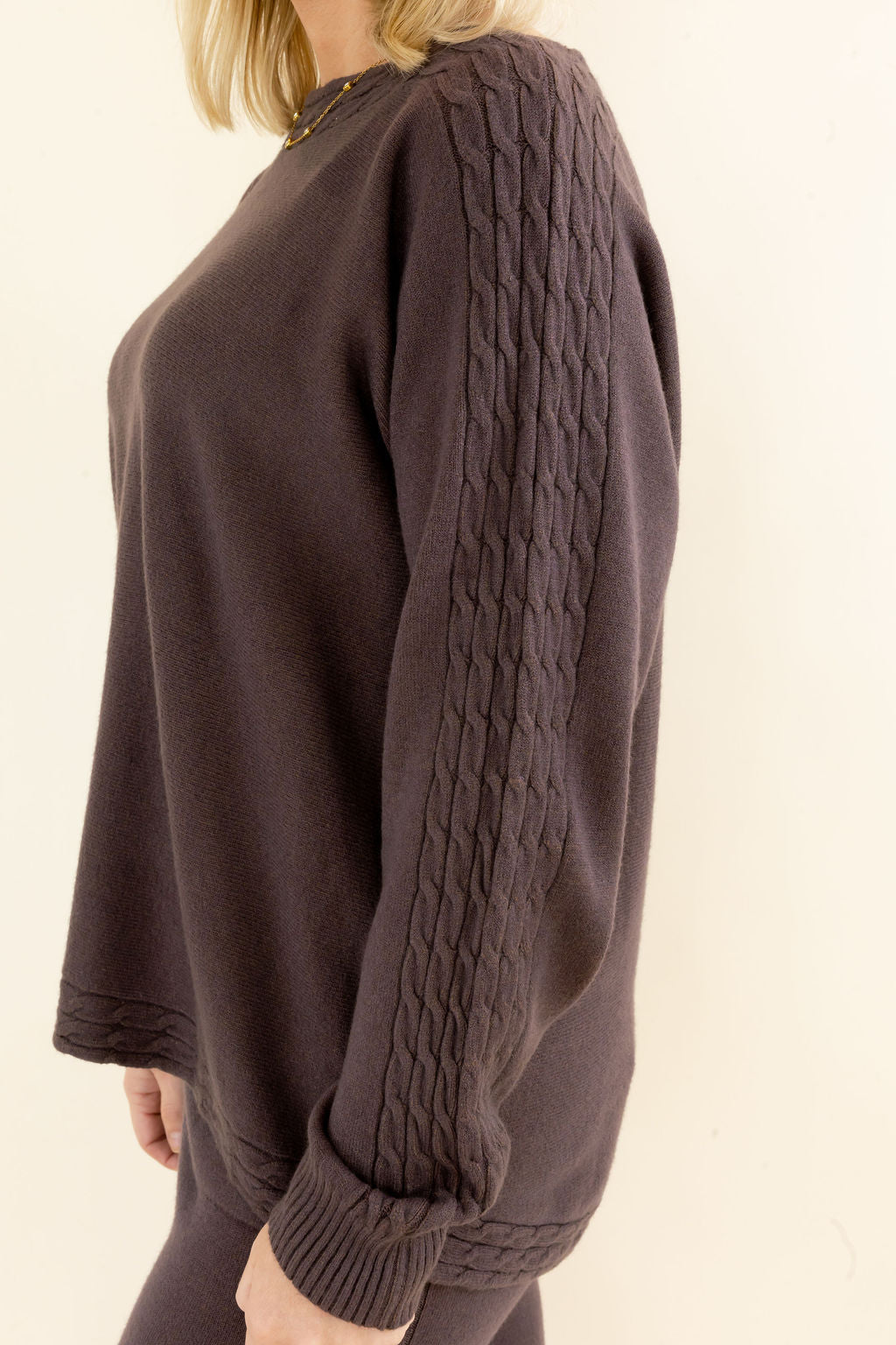 Close-up of chocolate brown knit pullover showing textured long sleeve detail, crew neckline, and soft relaxed silhouette