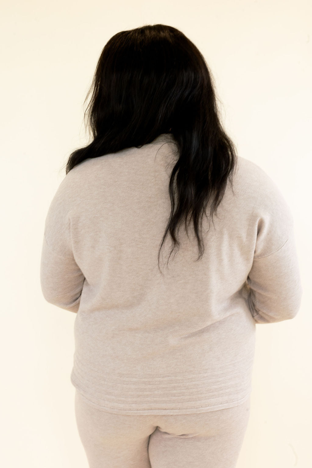 Back view of light taupe knit pullover showing long sleeves, soft textured fabric, relaxed fit, and ribbed hem