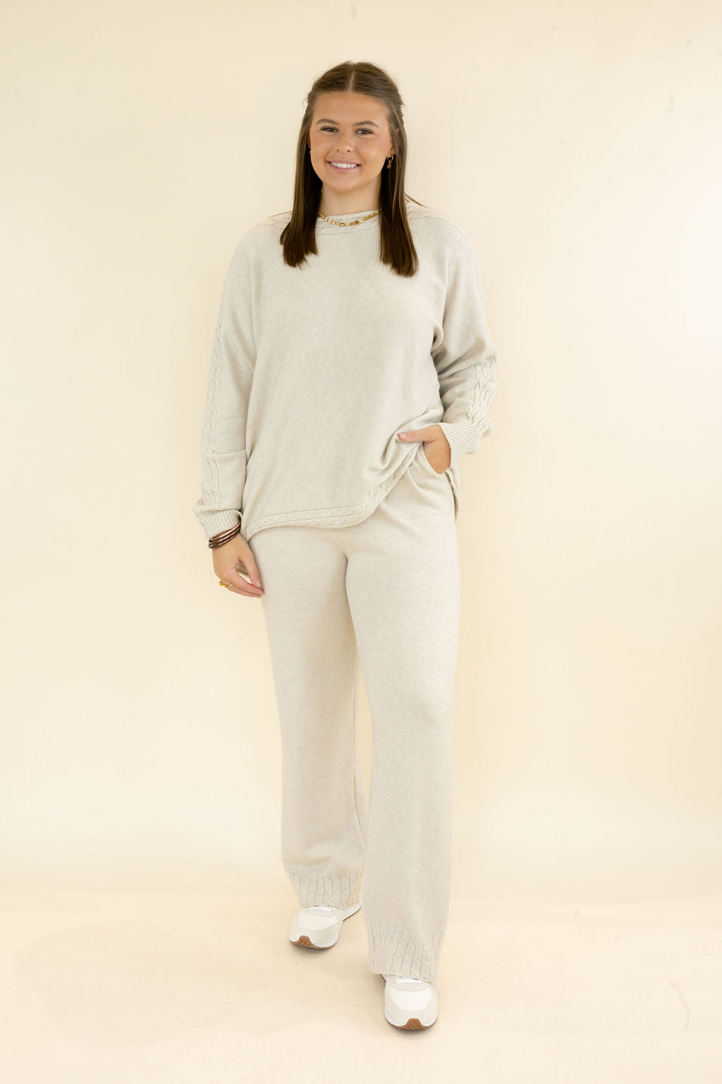 Woman modeling light oatmeal knit lounge set with long sleeve textured pullover top and matching relaxed wide leg pants styled with white sneakers