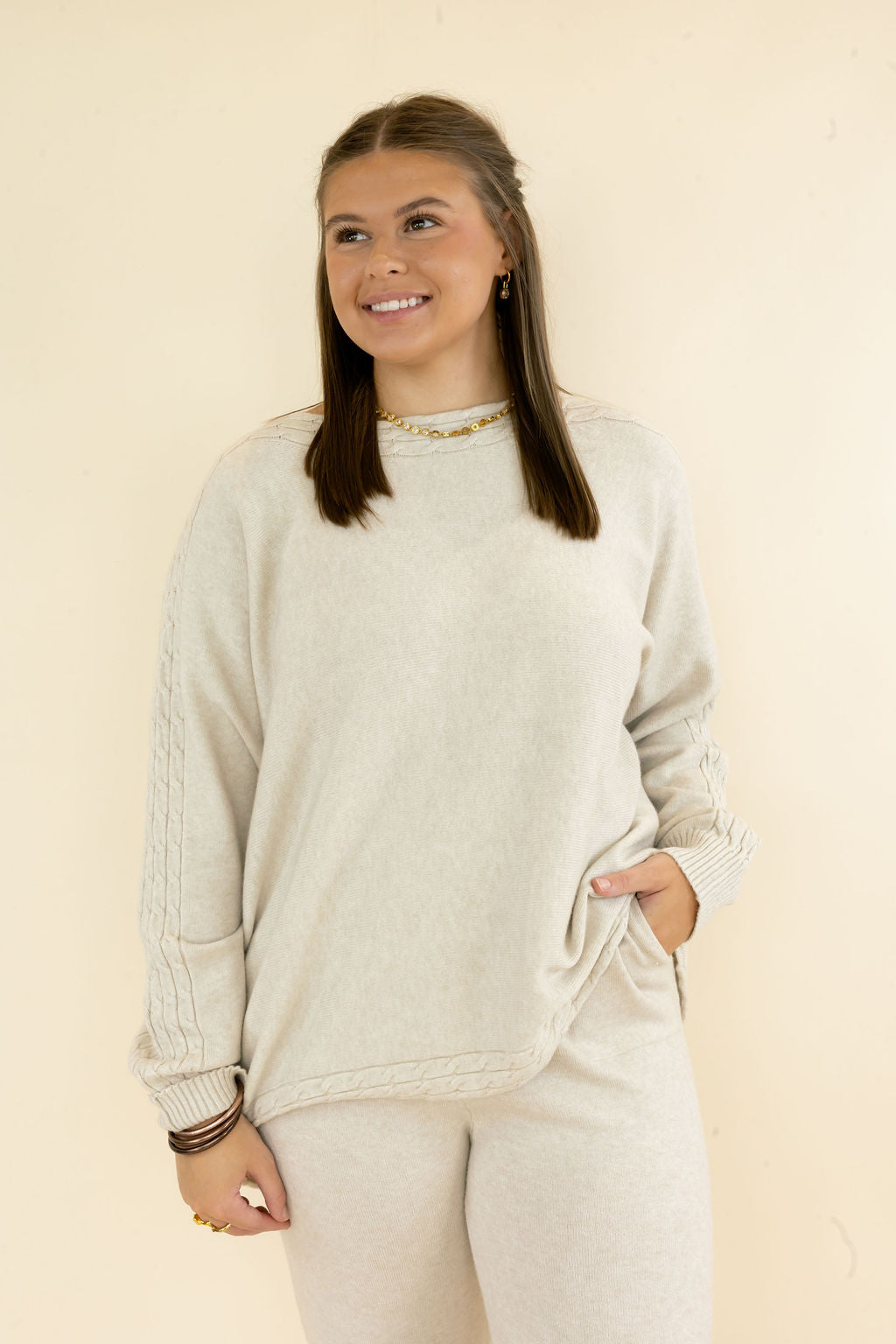 Front view of woman wearing light oatmeal textured knit pullover featuring crew neckline, long sleeves, relaxed fit, and matching pants