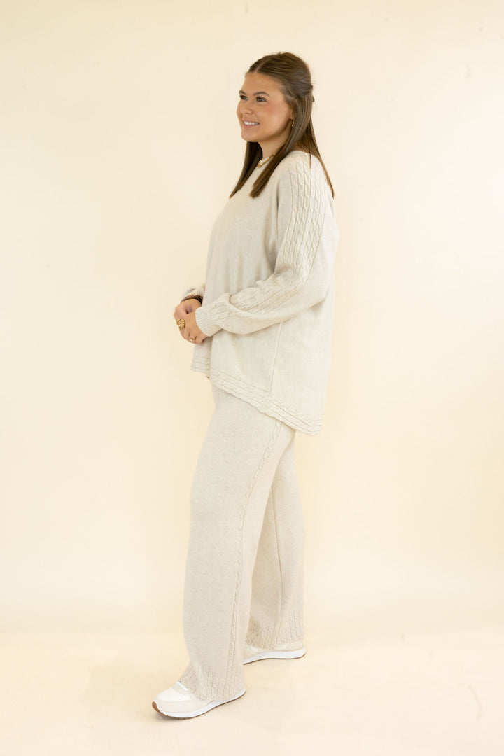 Side view of woman modeling light oatmeal knit lounge set featuring relaxed long sleeve top and matching wide leg pants