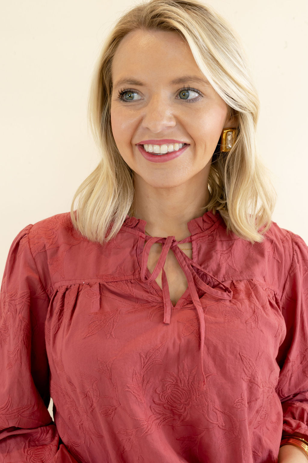 Close-up of rust red blouse highlighting the ruffled neckline, feminine tie-front detail, gathered fabric, and textured finish