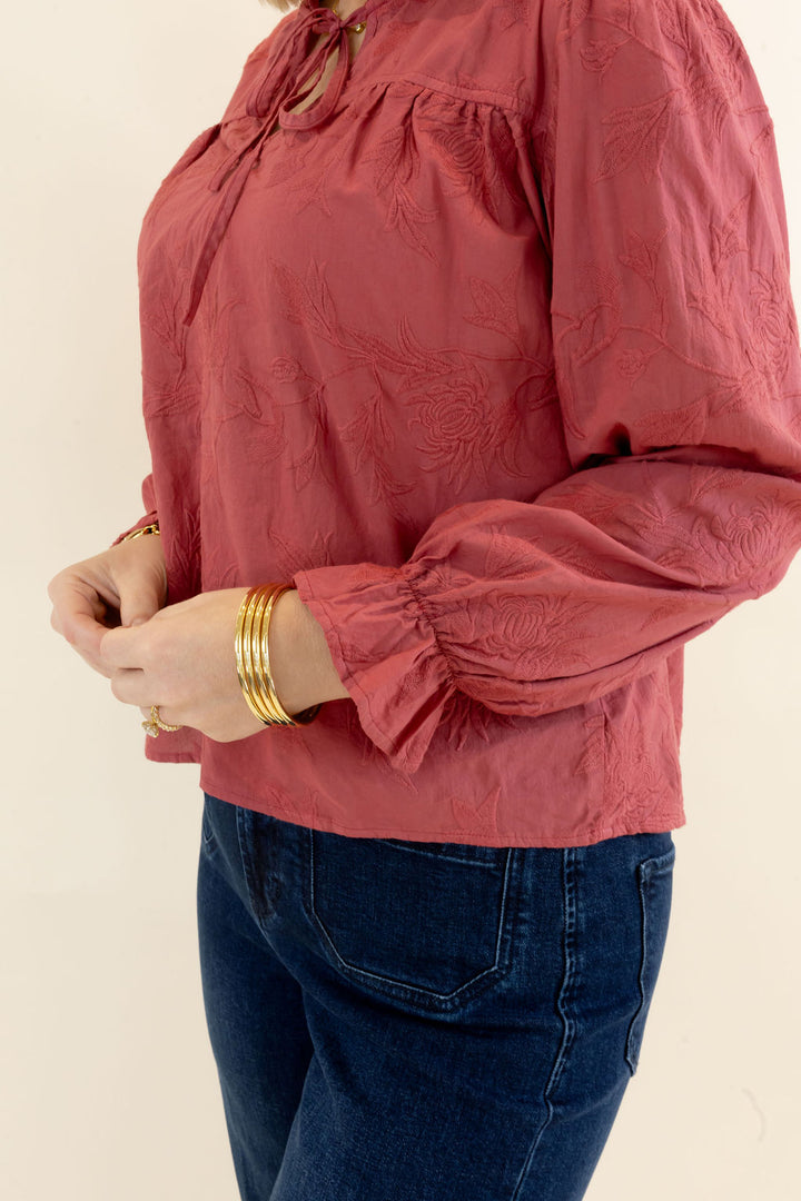 Side close-up of rust red blouse showing long balloon sleeve, gathered shoulder detail, and elastic ruffle cuff