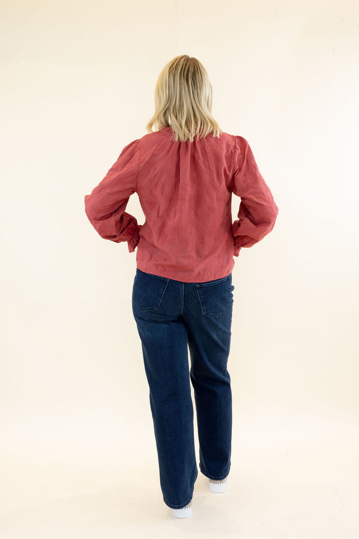 Full back view of woman wearing rust red long sleeve blouse with relaxed silhouette styled with dark wash wide leg jeans
