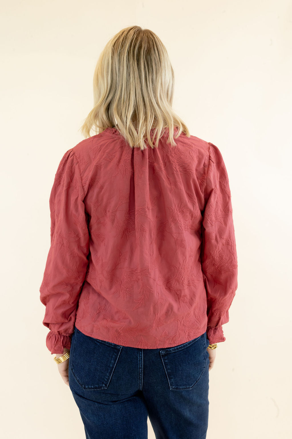 Back view of rust red long sleeve blouse showing gathered shoulder detailing, relaxed silhouette, and hip-length hem