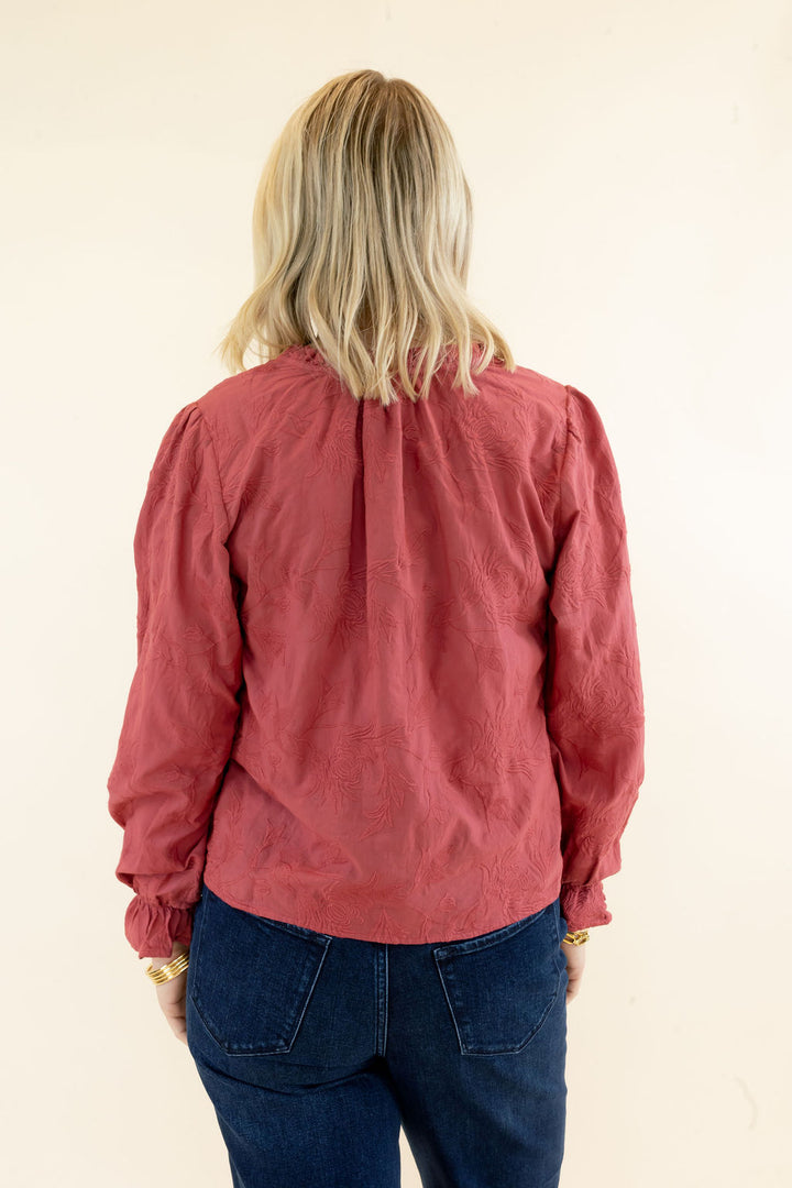 Back view of rust red long sleeve blouse showing gathered shoulder detailing, relaxed silhouette, and hip-length hem