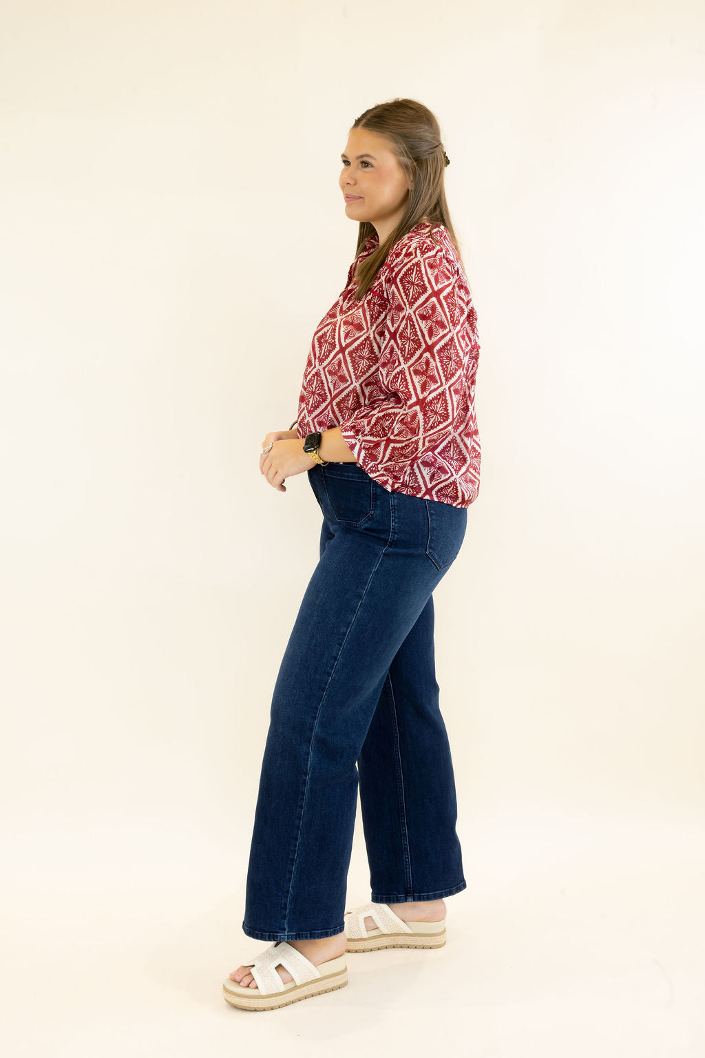 Side view of woman modeling red and ivory patterned blouse with three-quarter sleeves and dark wash wide leg jeans