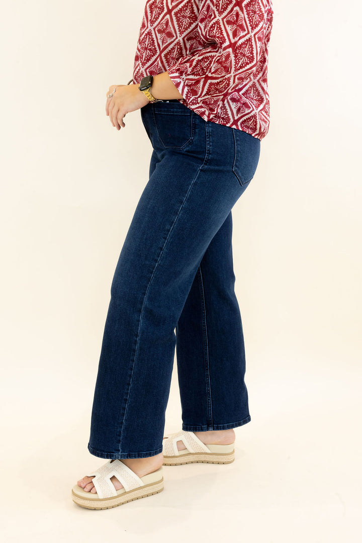 Side view of woman modeling dark wash wide leg jeans with relaxed fit and full-length hem styled with a red printed blouse