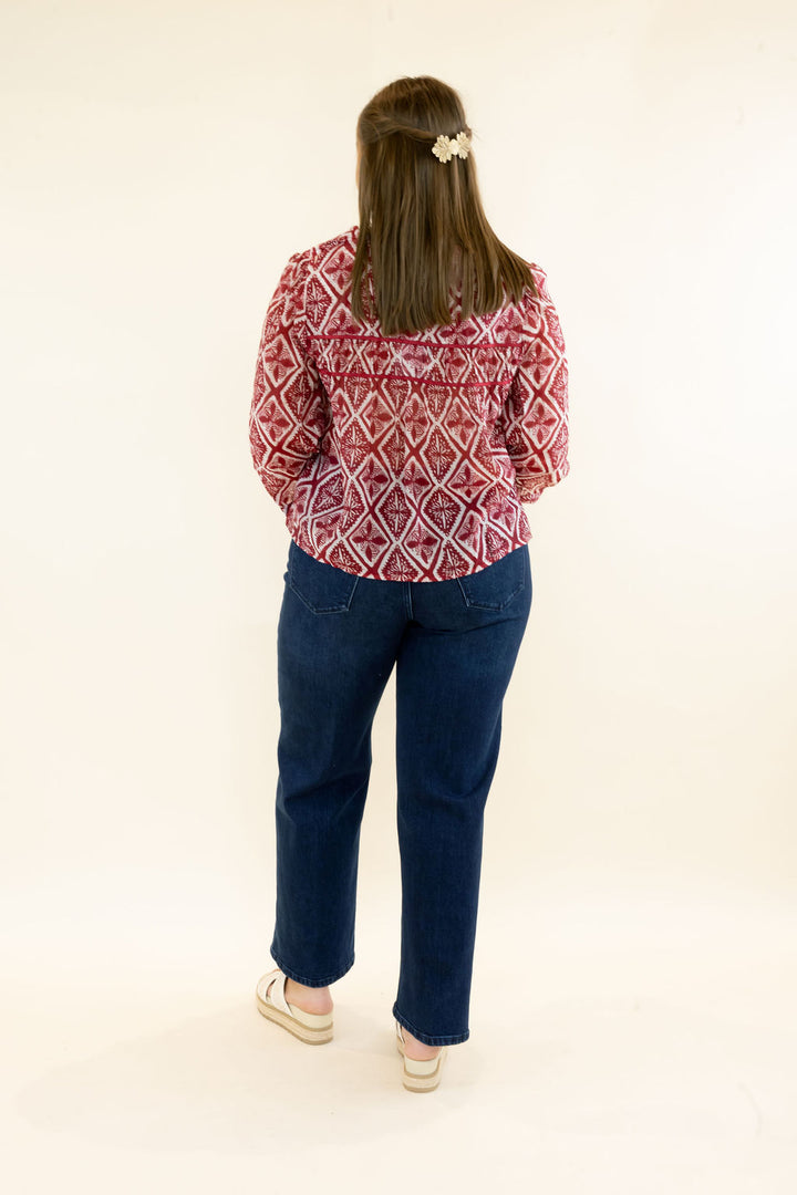 Full back view of woman wearing red and ivory geometric print blouse showing the relaxed silhouette and dark wash jeans
