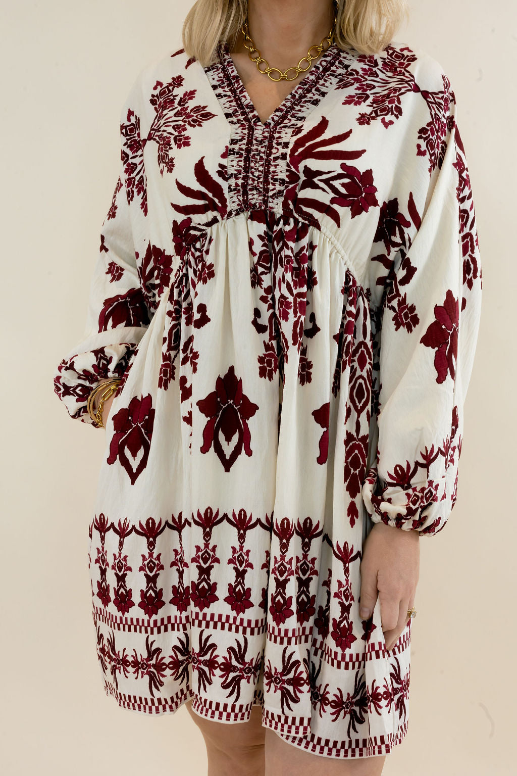 Close-up of ivory mini dress highlighting the burgundy botanical print, V-neckline, decorative trim, gathered waist, and long balloon sleeves