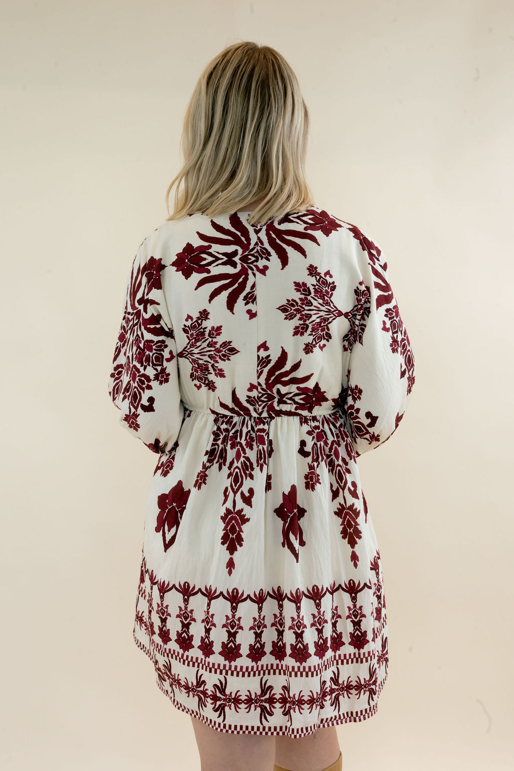 Back view of ivory and burgundy botanical print mini dress showing the long sleeves, relaxed gathered silhouette, and coordinating border print hem
