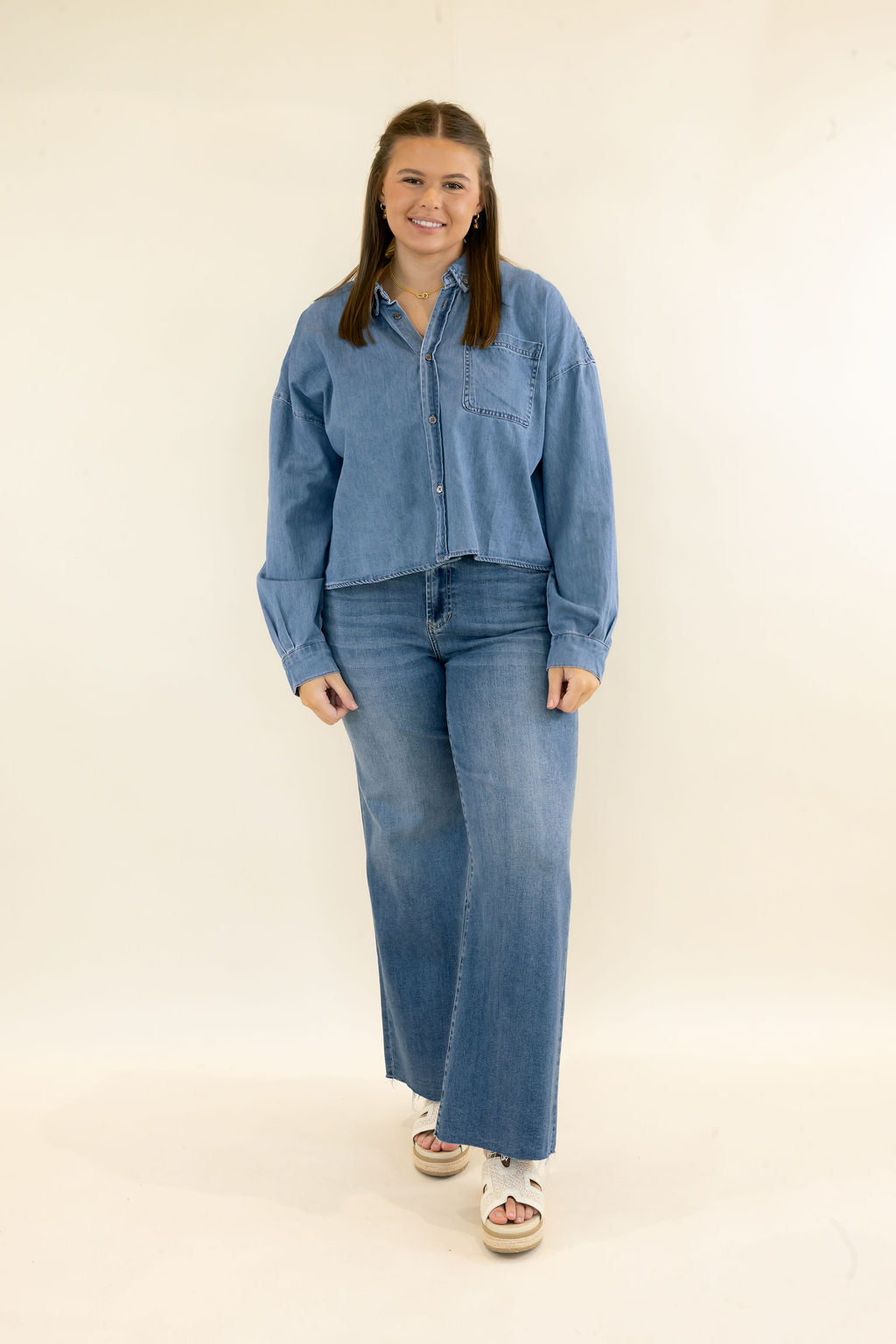 Woman modeling light wash denim button-up shirt with long sleeves, chest pocket, relaxed fit, and matching wide leg jeans