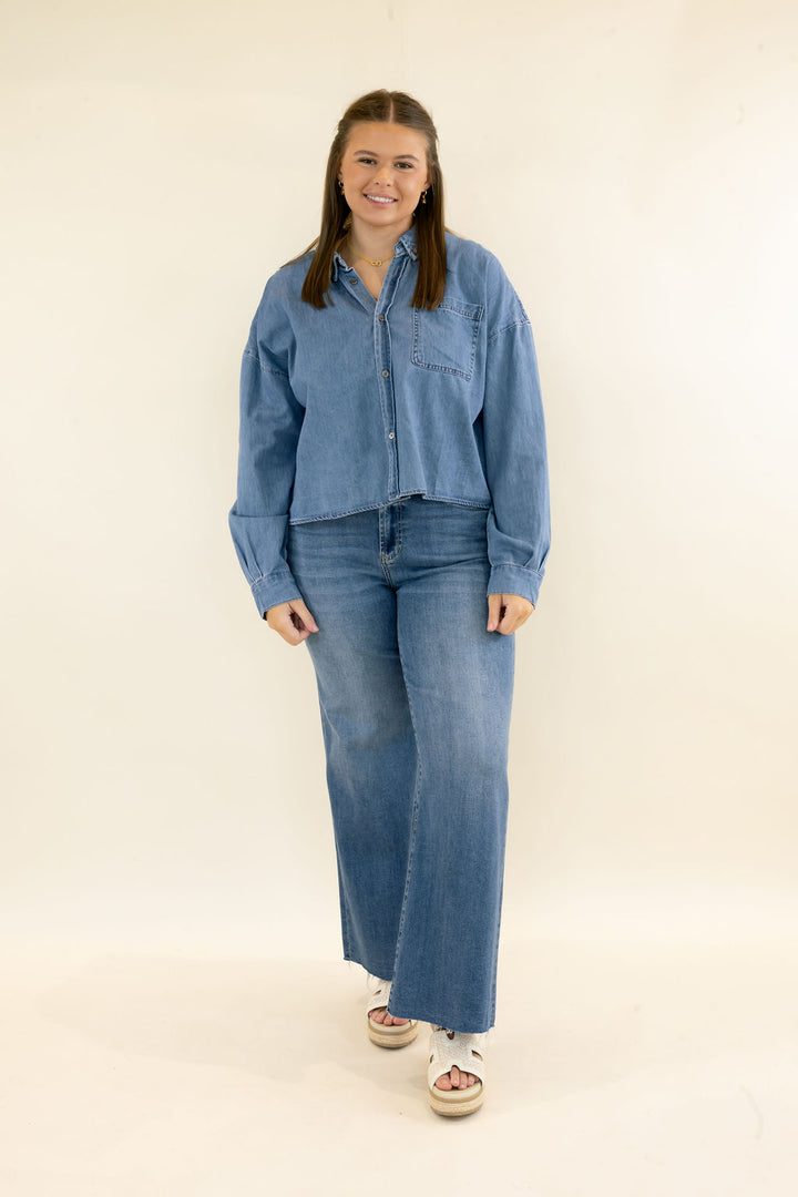 Woman modeling light wash denim button-up shirt with long sleeves, chest pocket, relaxed fit, and matching wide leg jeans