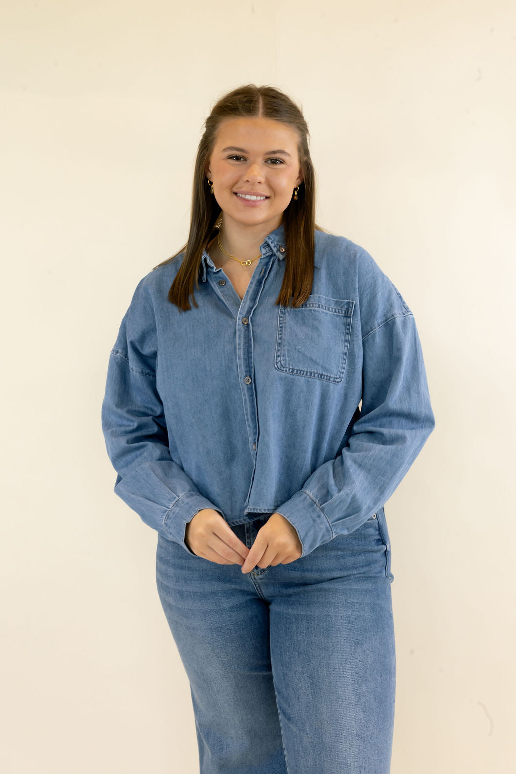 Woman wearing light blue denim button-down shirt with relaxed fit, curved hem, and coordinating wide leg jeans