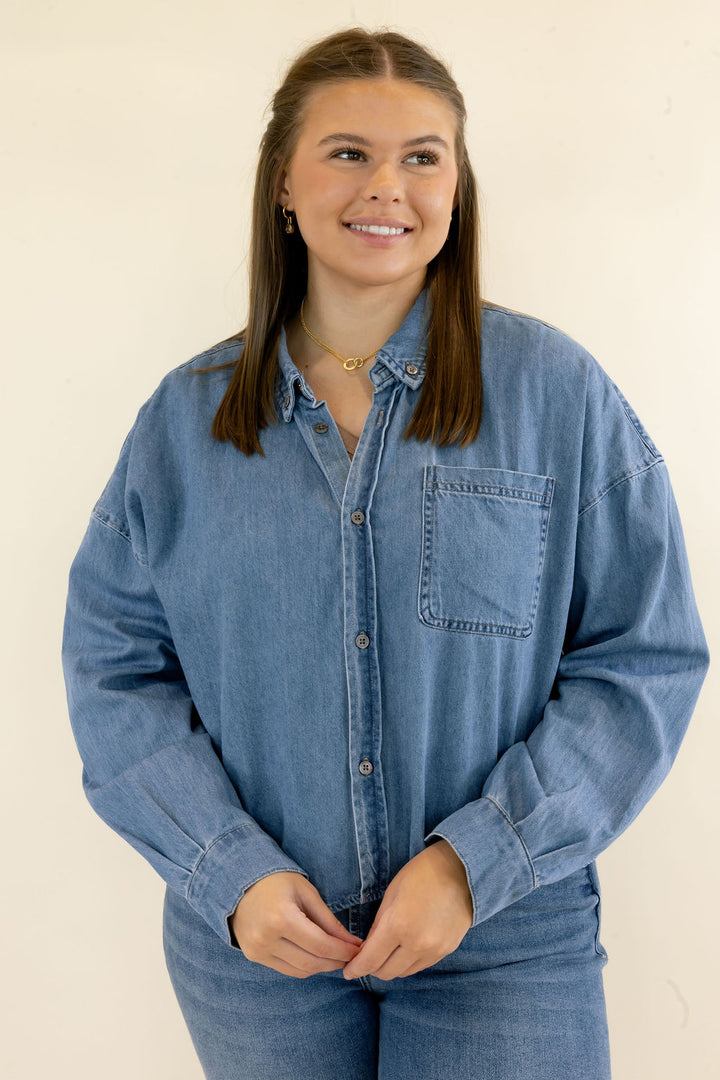 Front view of light wash denim button-up shirt featuring collared neckline, chest pocket, long sleeves, and relaxed silhouette