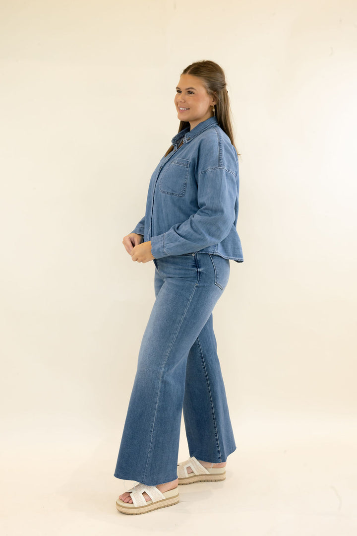 Side view of woman modeling light wash denim button-up shirt with matching wide leg jeans and neutral platform sandals