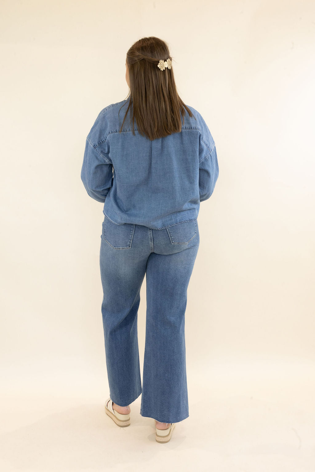 Full back view of woman wearing light wash denim button-up shirt and coordinating wide leg jeans showing the relaxed denim-on-denim look