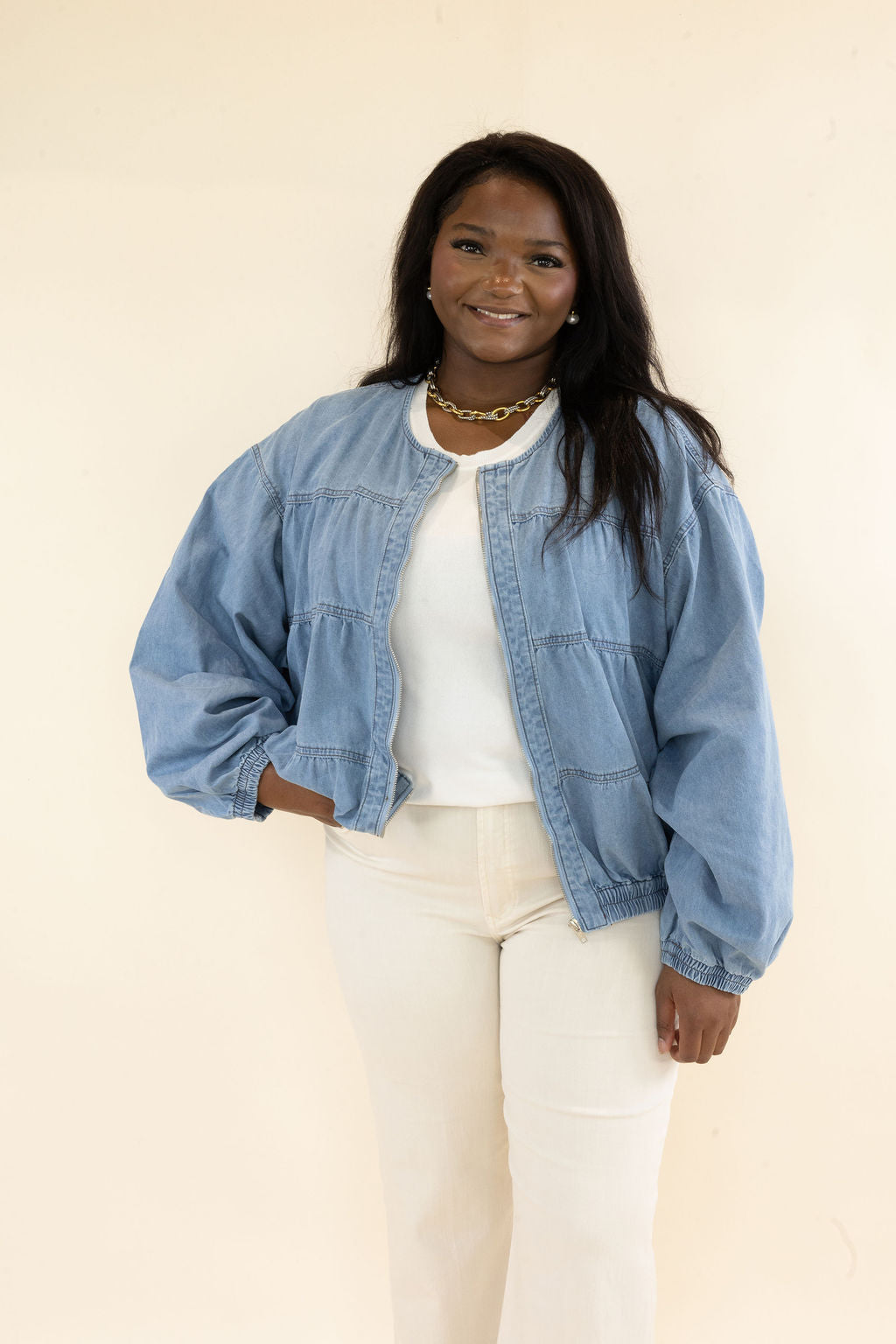 Woman modeling light blue denim bomber jacket featuring snap button front, oversized sleeves, and relaxed cropped silhouette
