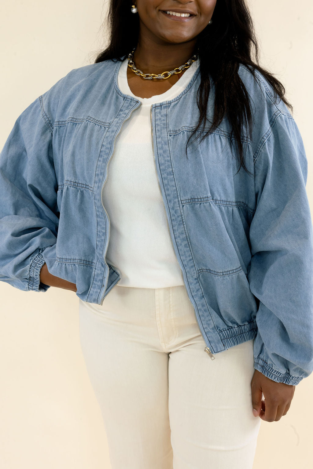 Close-up of light wash denim bomber jacket showing snap button closure, gathered seam detailing, balloon sleeves, and elastic hem