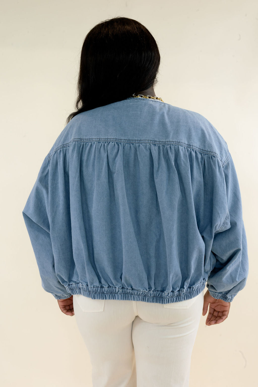 Back view of light wash denim bomber jacket showing gathered yoke detail, oversized balloon sleeves, and elasticized hem
