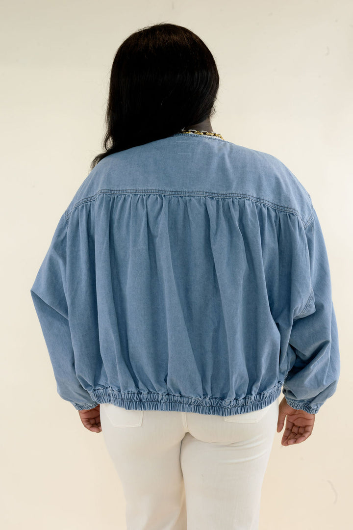 Back view of light wash denim bomber jacket showing gathered yoke detail, oversized balloon sleeves, and elasticized hem