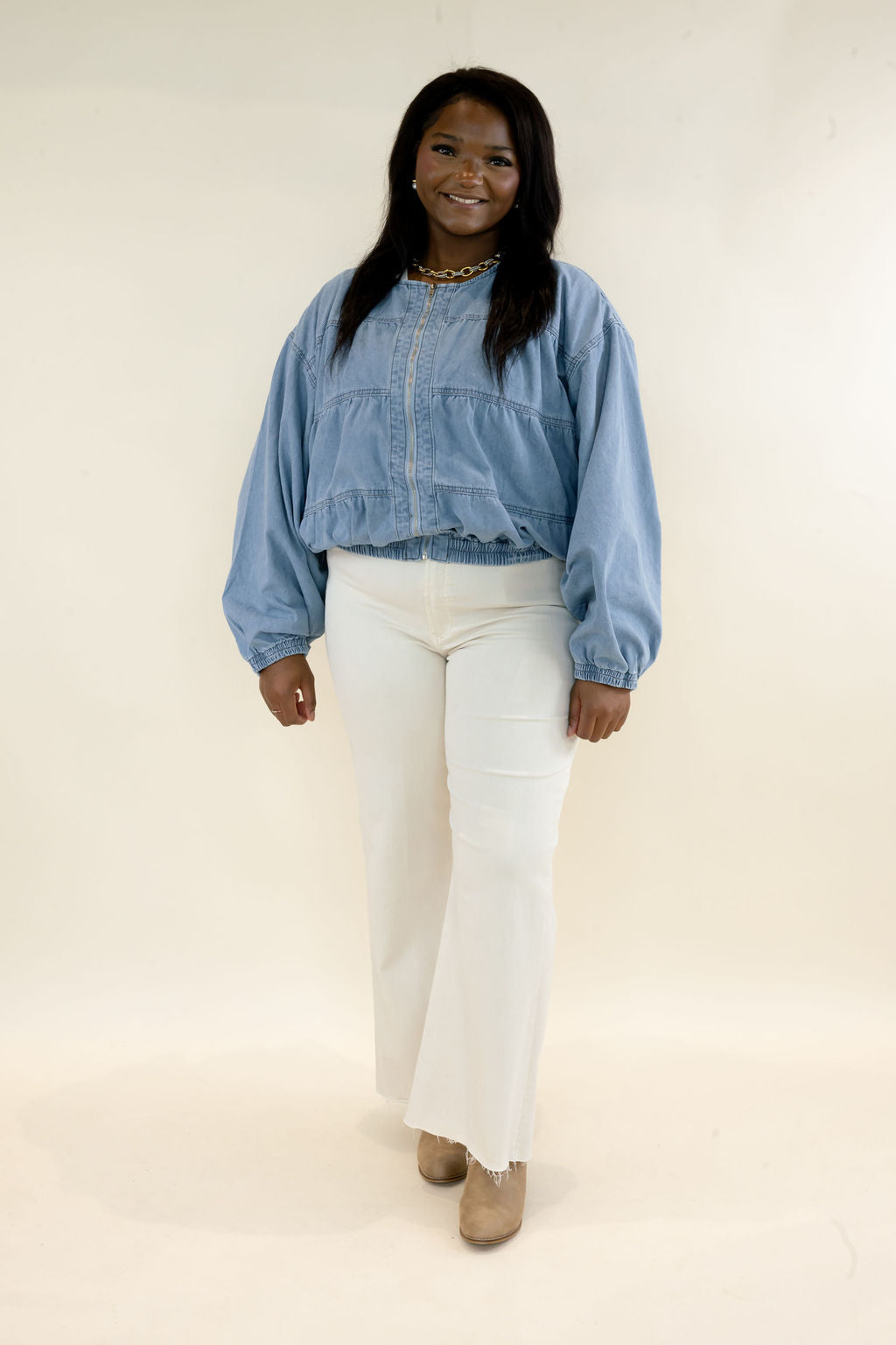 Woman modeling light wash denim bomber jacket with snap button front and balloon sleeves styled with white straight leg pants