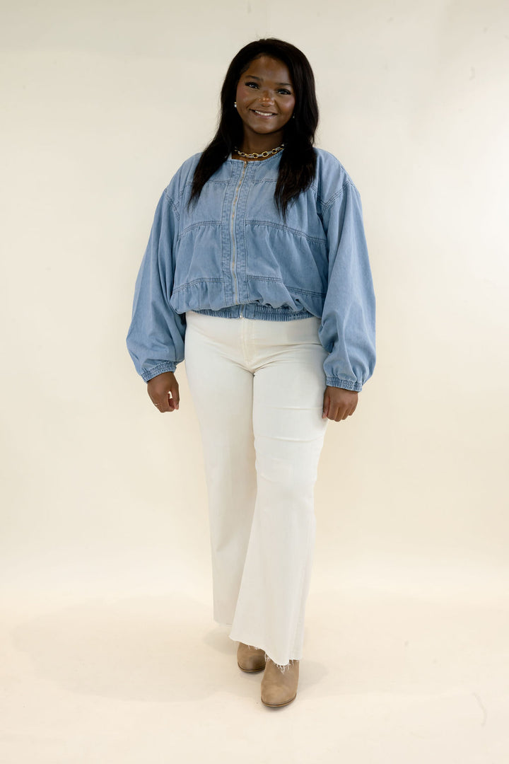 Woman modeling light wash denim bomber jacket with snap button front and balloon sleeves styled with white straight leg pants
