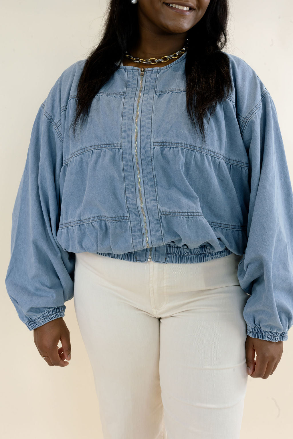 Front view of light blue denim bomber jacket highlighting the snap button closure, gathered bodice, long balloon sleeves, and elasticized hem