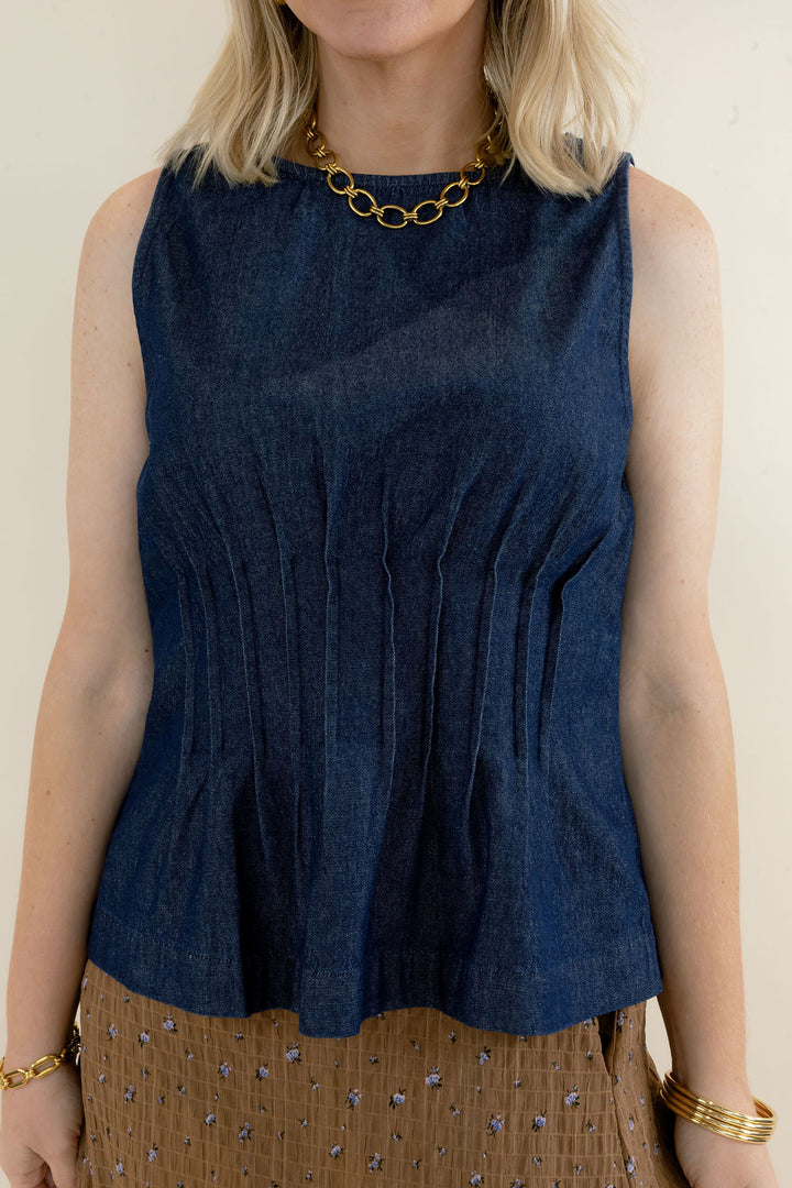 Close-up of dark indigo sleeveless denim top highlighting the round neckline, vertical pleat detailing, fitted waist, and flared peplum hem