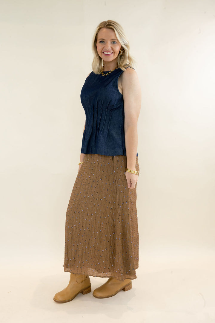 Side view of woman modeling dark indigo sleeveless denim peplum top with brown midi skirt and tan ankle boots