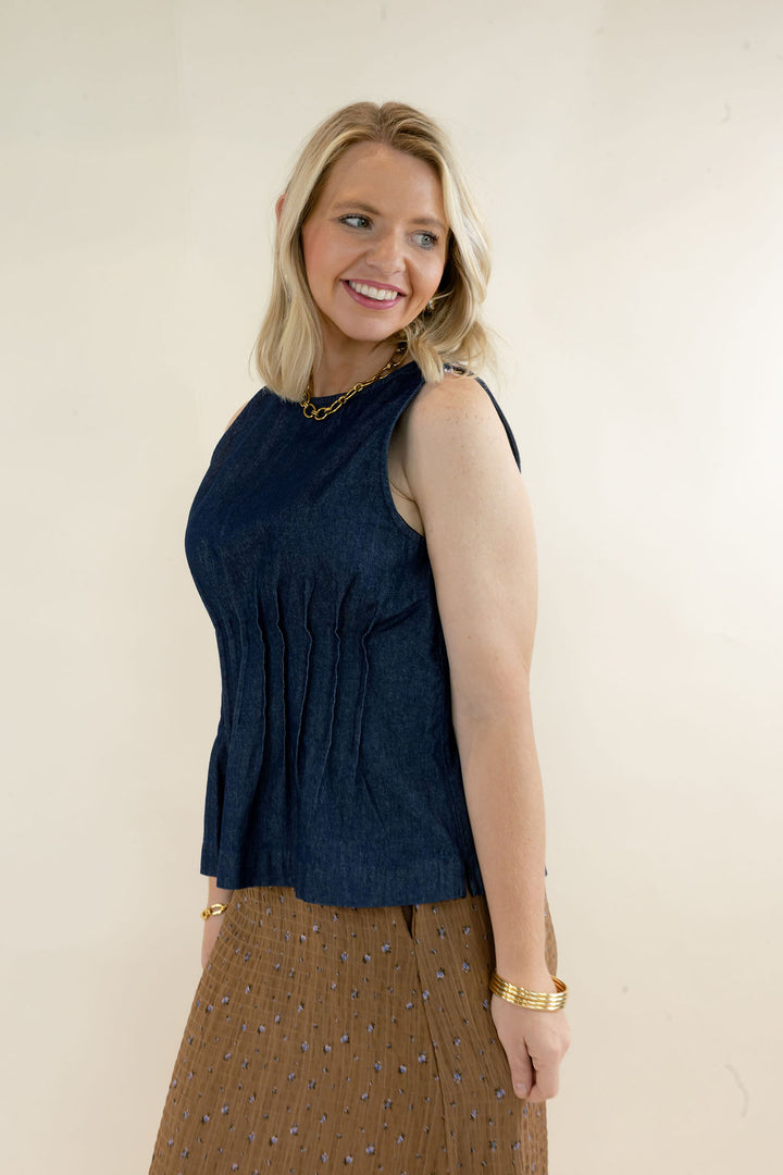Three-quarter view of dark indigo sleeveless denim top featuring a fitted pleated bodice, round neckline, and flared peplum silhouette