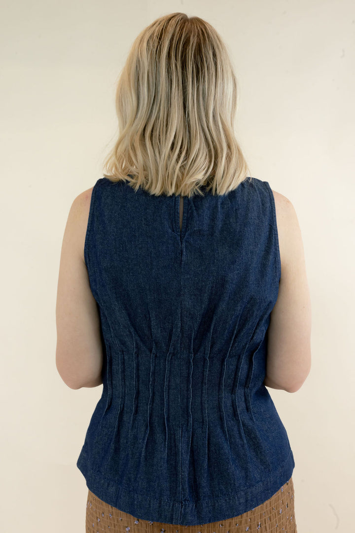 Back view of dark indigo sleeveless denim peplum top showing vertical pleat detailing, fitted waist, and flared hem