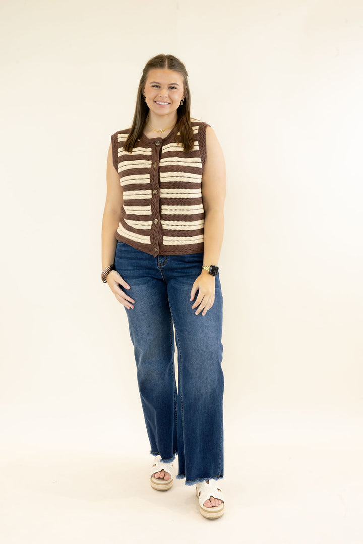 Full-length view of woman wearing brown and cream striped button-front sweater vest styled with dark wash wide leg jeans