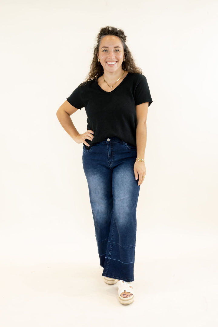 Woman modeling EverStretch indigo dark denim wide crop jeans with release hem and faded wash styled with a black V-neck tee and neutral platform sandals