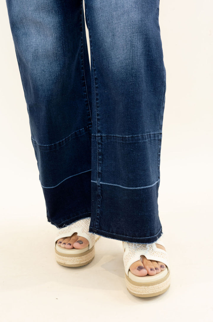 Close-up of EverStretch indigo dark denim wide crop jeans highlighting the lower leg seam detailing, released raw hem, and dark wash