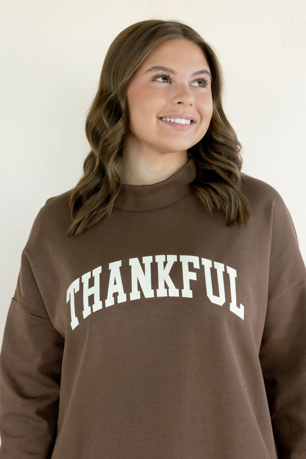 Close-up of brown Thankful reversible mockneck sweatshirt showing white varsity-style lettering and Word Warriors sleeve label