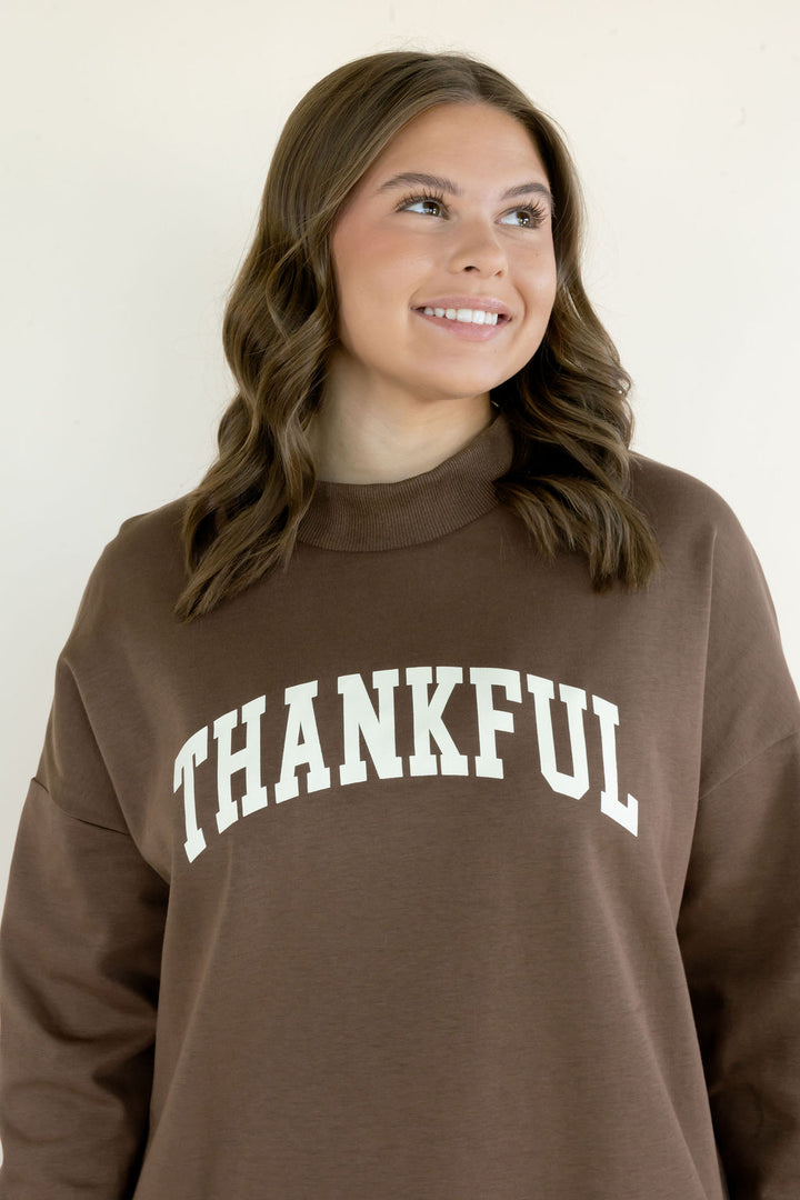 Close-up of brown Thankful reversible mockneck sweatshirt showing white varsity-style lettering and Word Warriors sleeve label