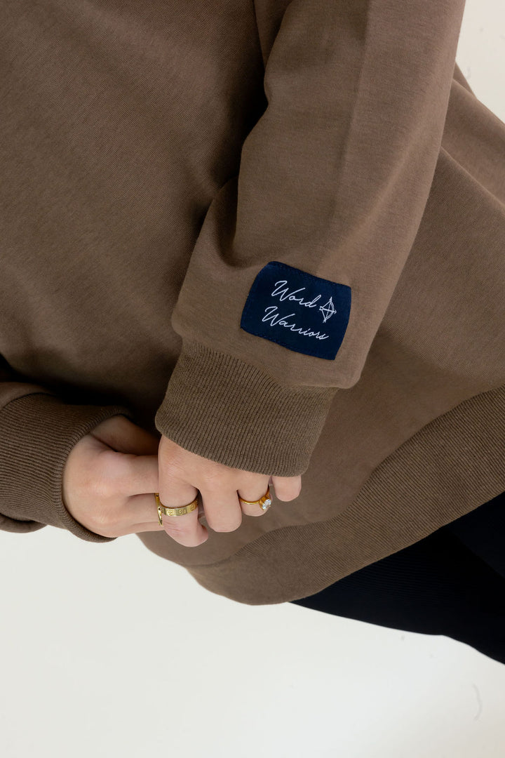 Close-up of brown Reversible Thankful &amp; Blessed Mockneck Sweatshirt showing the Word Warriors brand label at the sleeve cuff