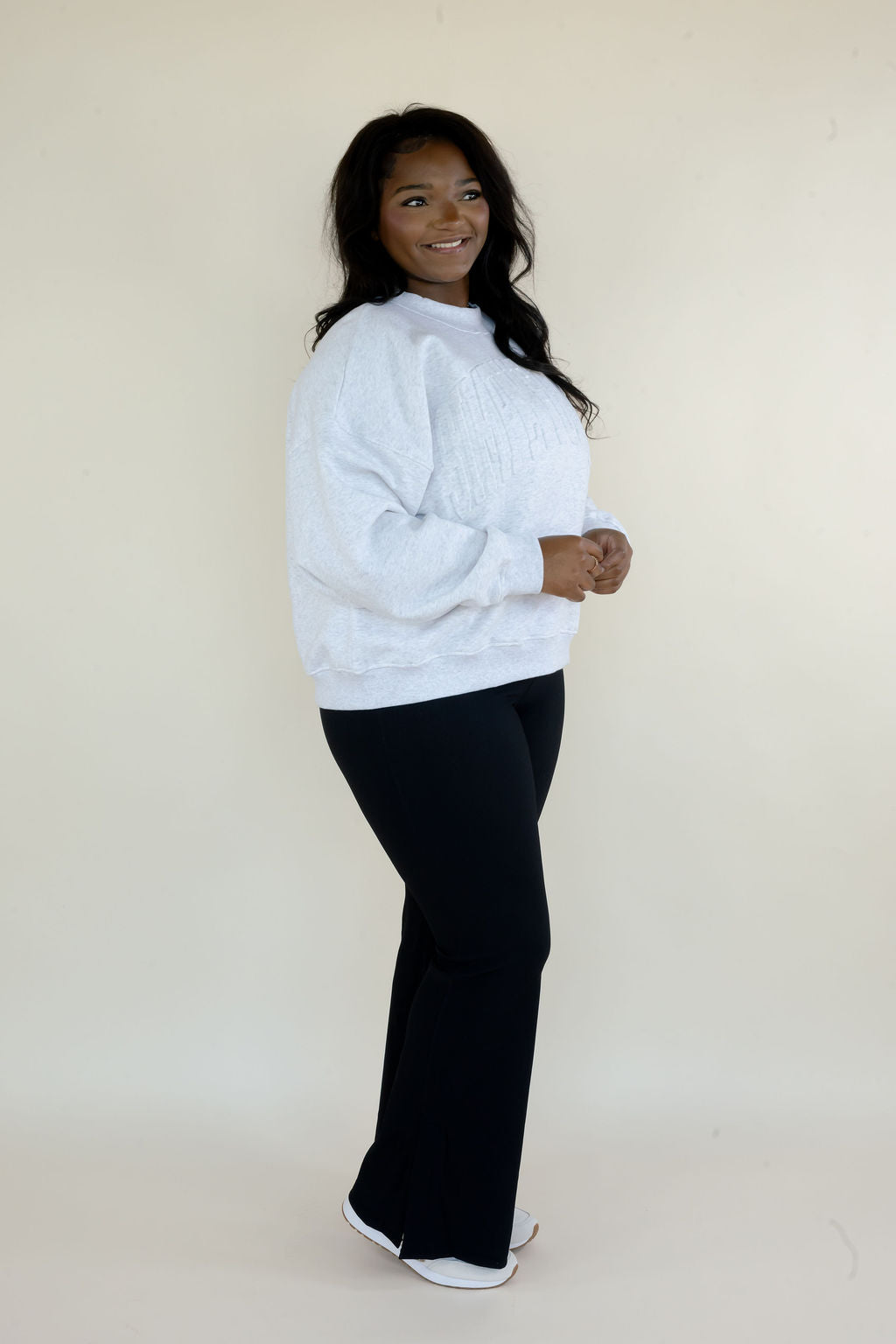 Side view of woman wearing heather gray Simply For Good sweatshirt with relaxed fit and black flare pants
