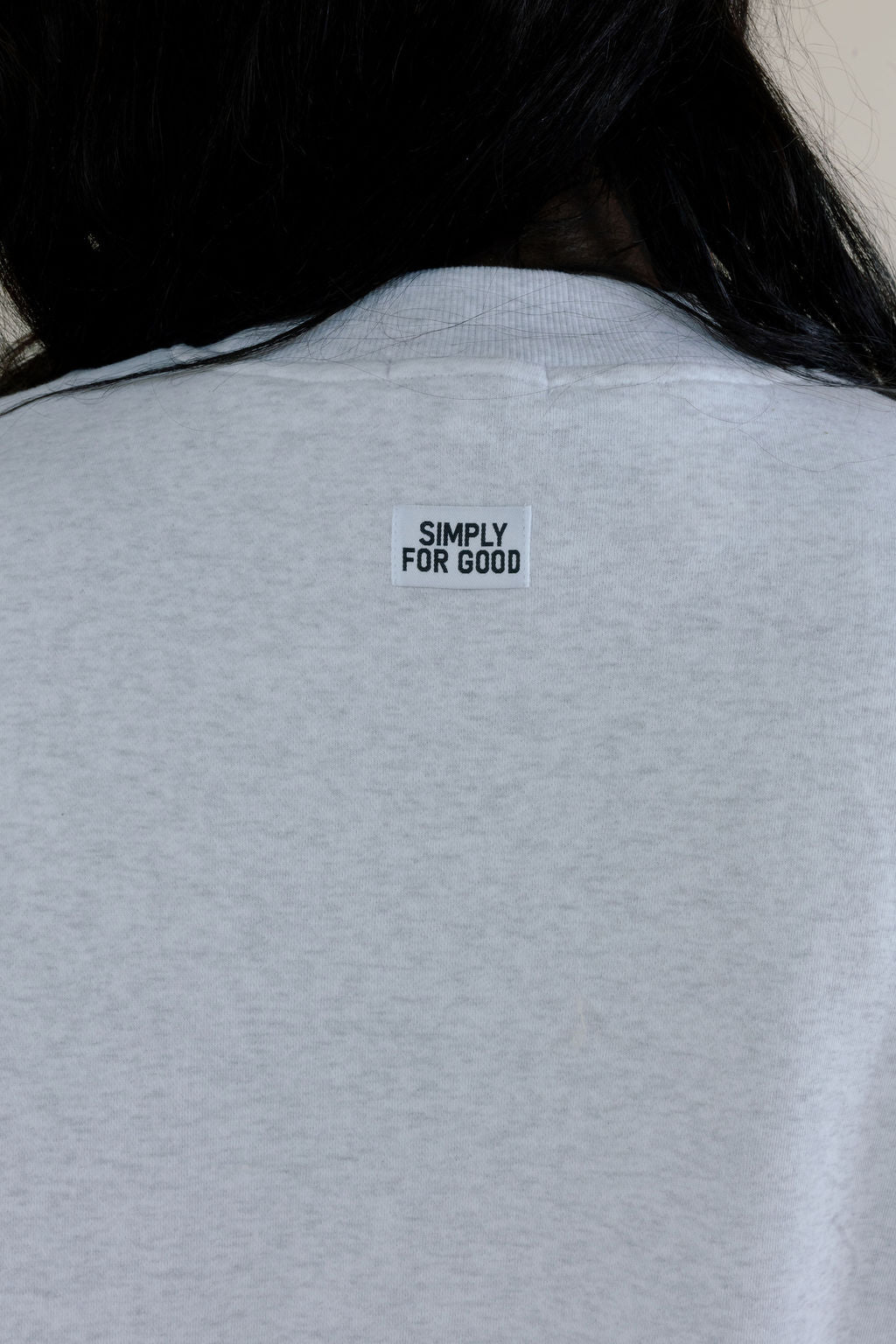 Close-up of heather gray sweatshirt showing small Simply For Good branding centered below the back neckline