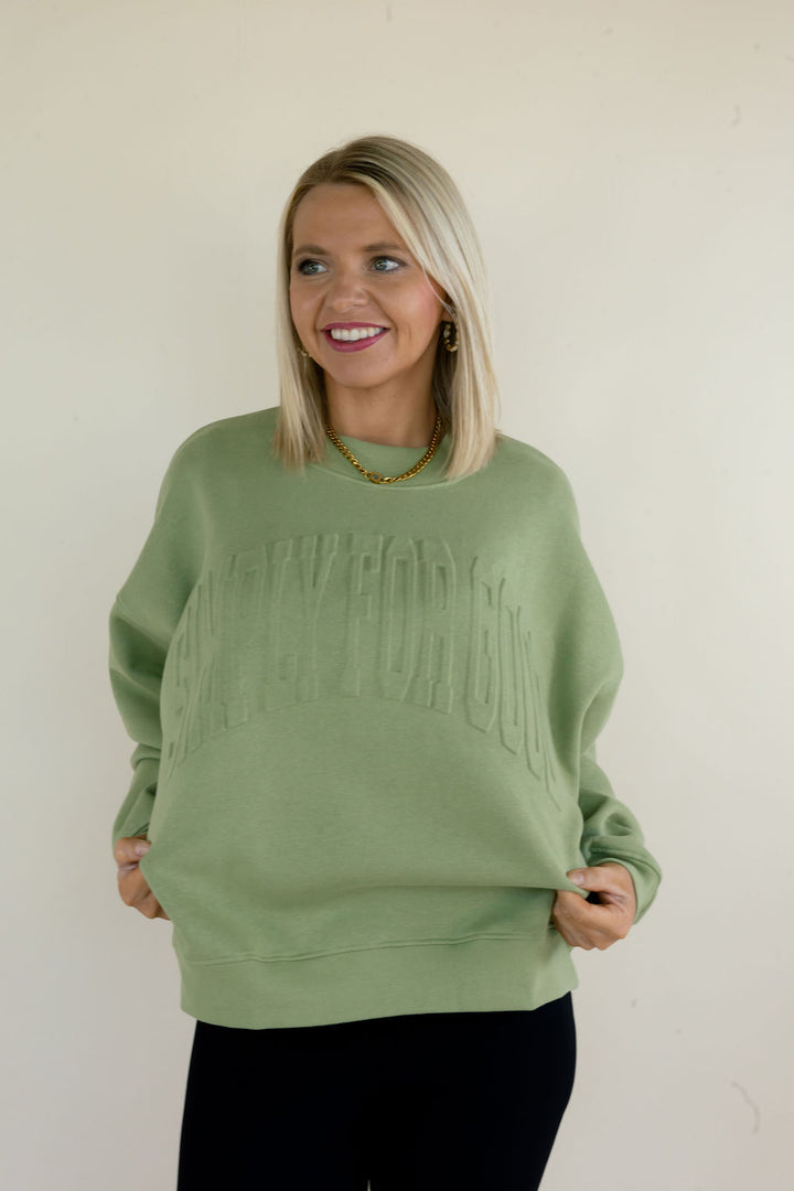 Front view of sage green Simply For Good sweatshirt showing tonal raised lettering, crew neckline, and relaxed fit