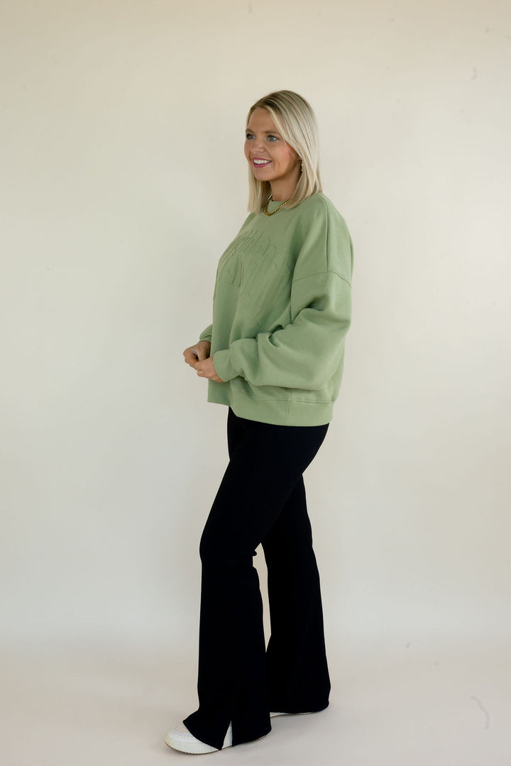 Side view of woman modeling sage green Simply For Good crewneck sweatshirt with black flare pants